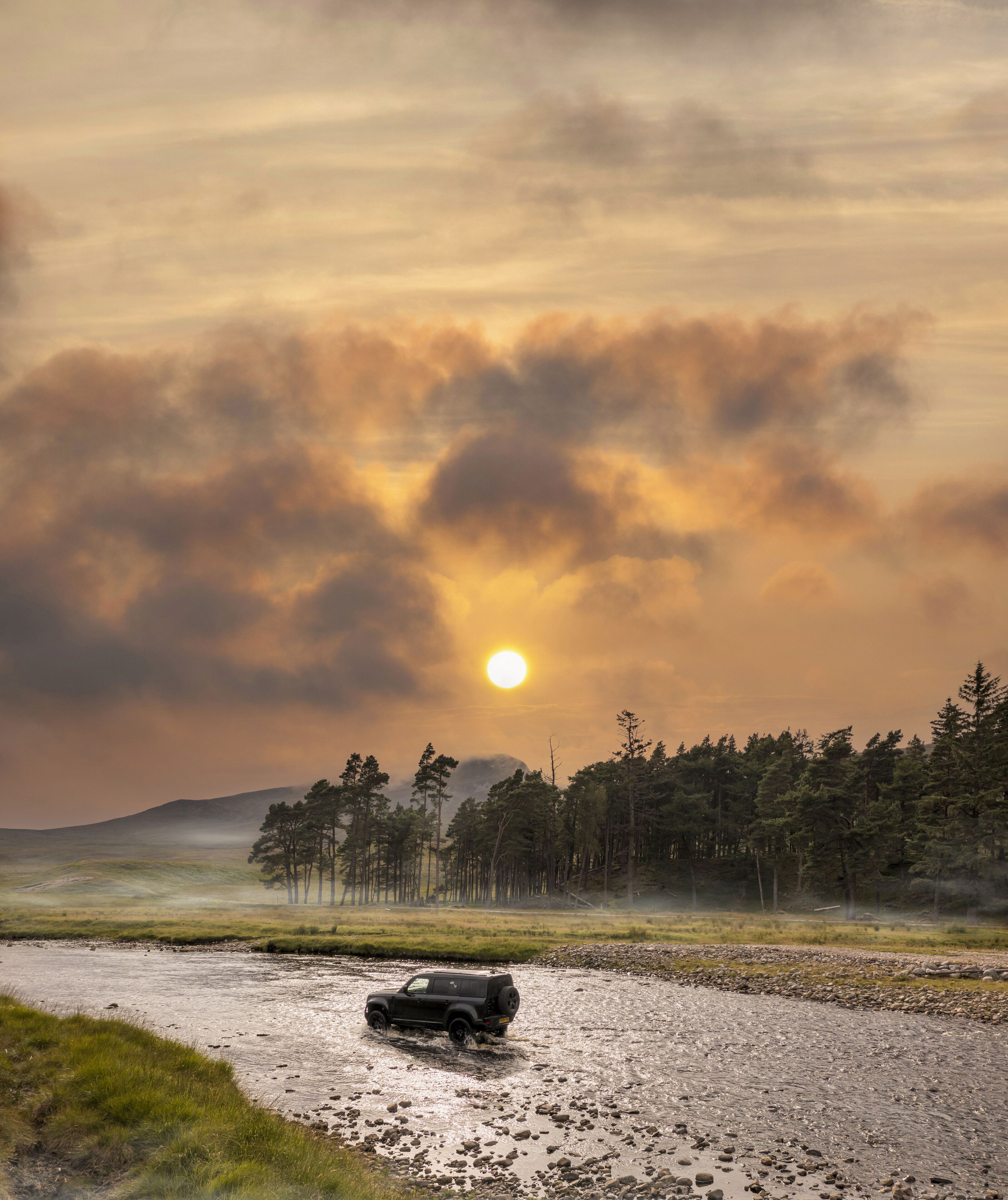 Aerial view of a lone vehicle braving the shallow waters near Ardverikie Estate under a fiery sunset, Newtonmore, Scotland, United Kingdom.