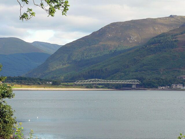 A bridge over a calm lake with mountains in the background.
