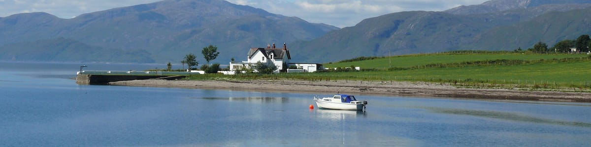 Un lac paisible avec une petite barque, une maison blanche et des montagnes en arrière-plan.
