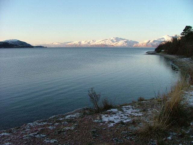Um lago tranquilo com montanhas cobertas de neve ao fundo.