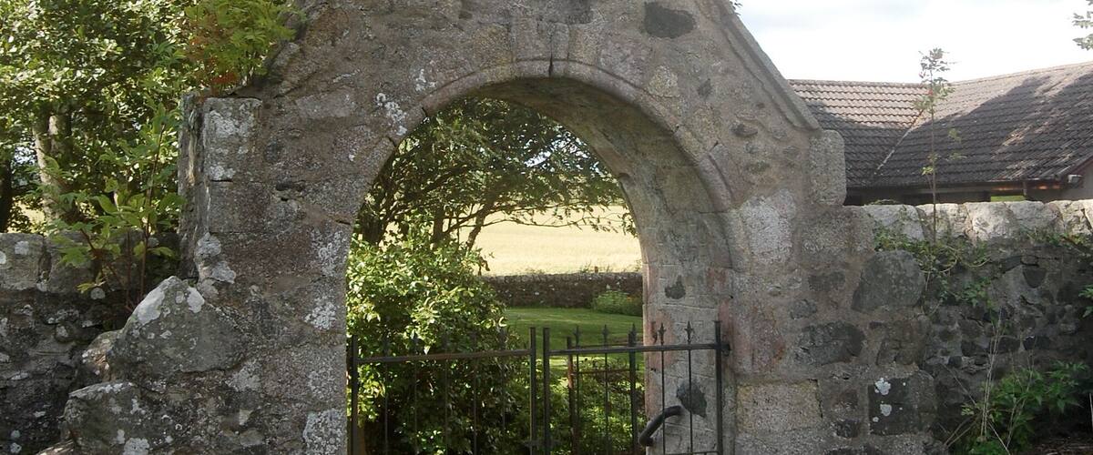 A stone archway with a metal gate, surrounded by greenery and a stone wall.