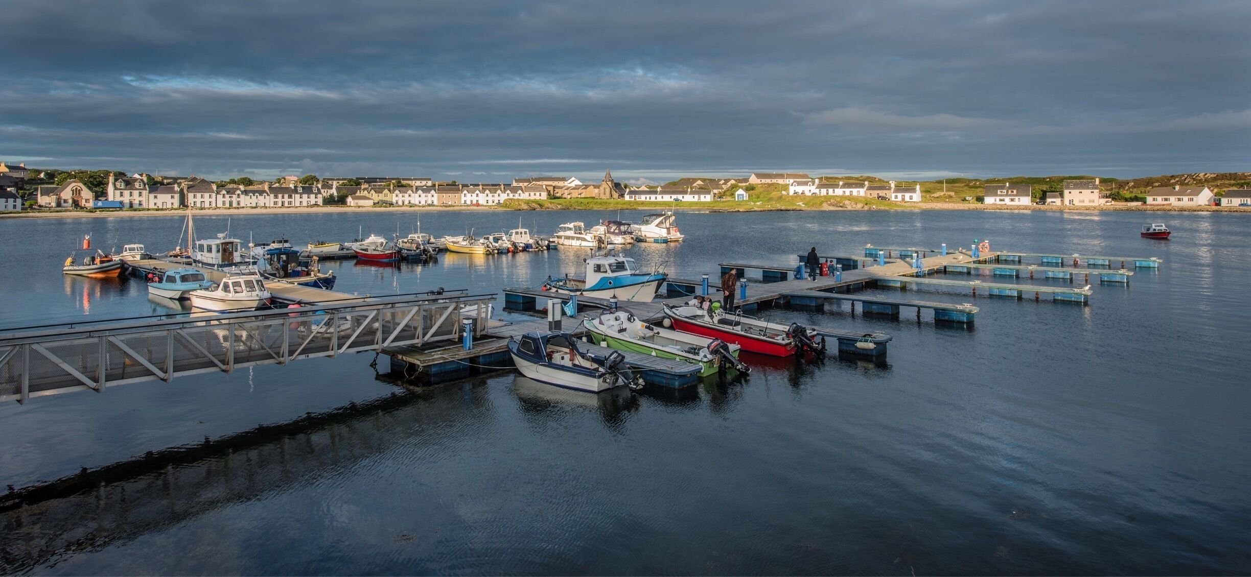 A harbor with various boats docked, a pier, and buildings in the background.
