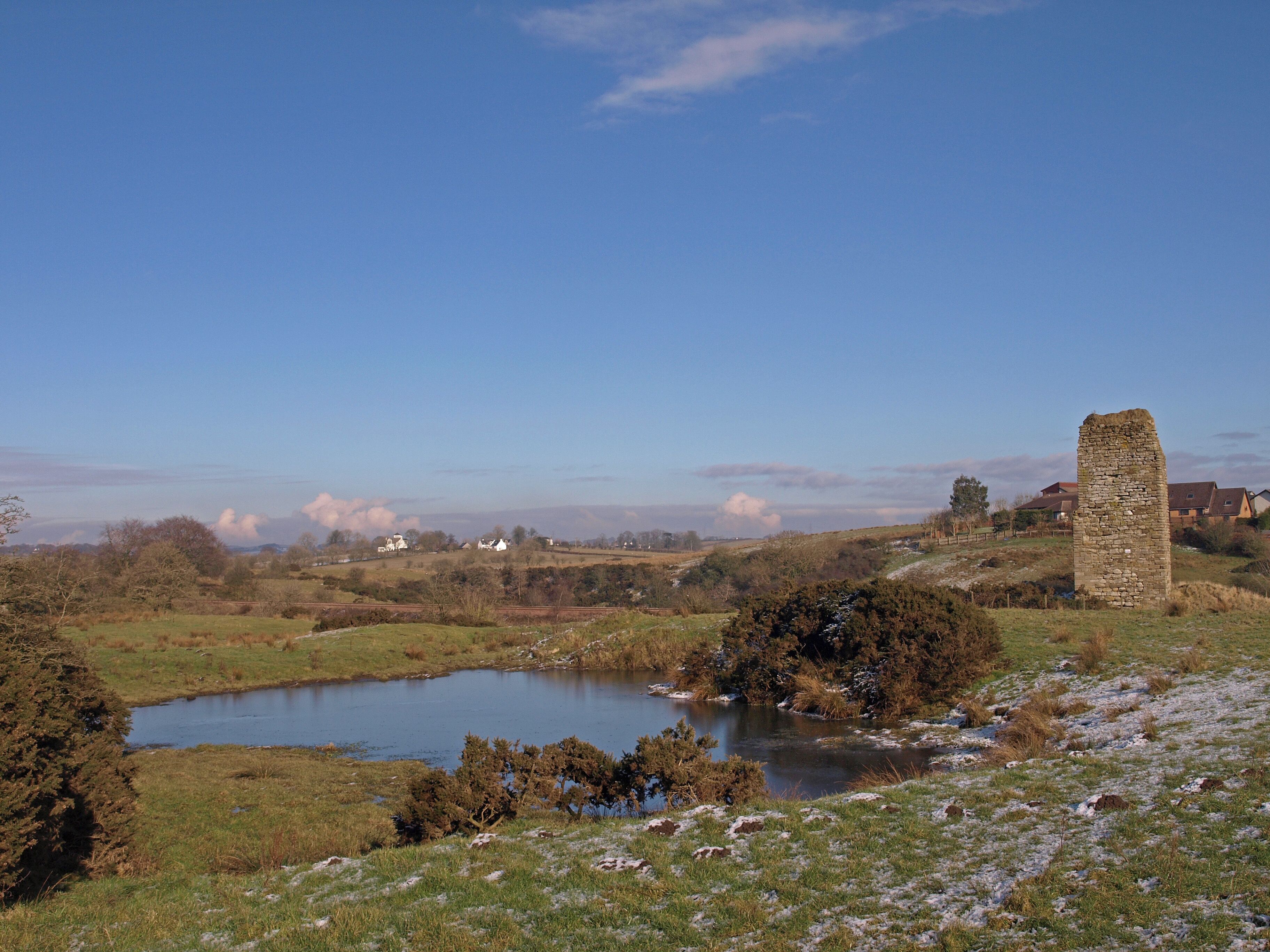 A stone tower, a pond, and houses in a rural landscape.