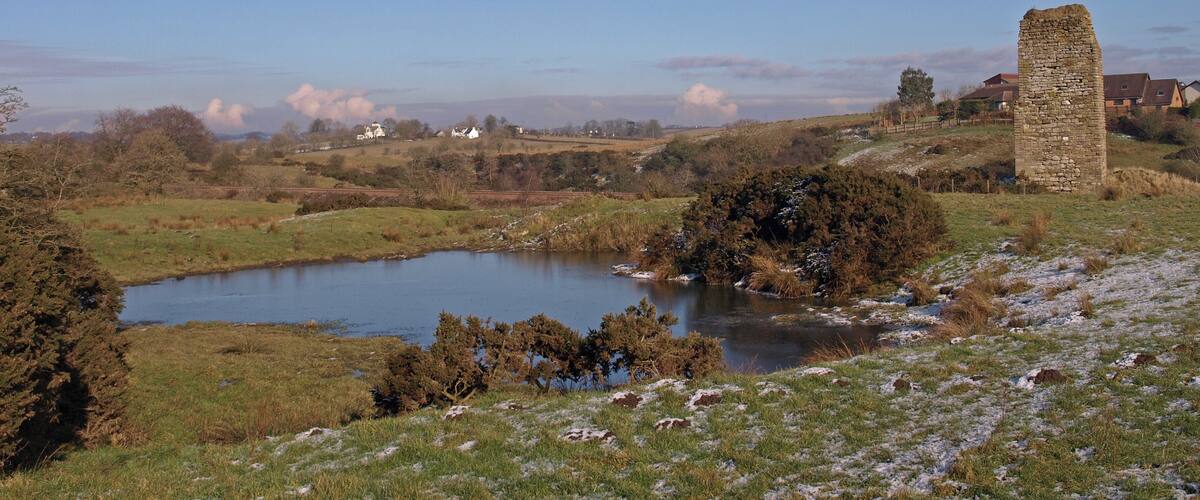 A stone tower, a pond, and houses in a rural landscape.