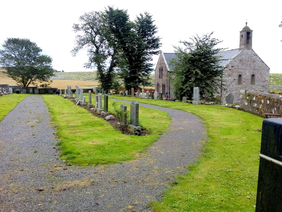 A cemetery with a winding path, stone headstones, and a church with a stone tower.