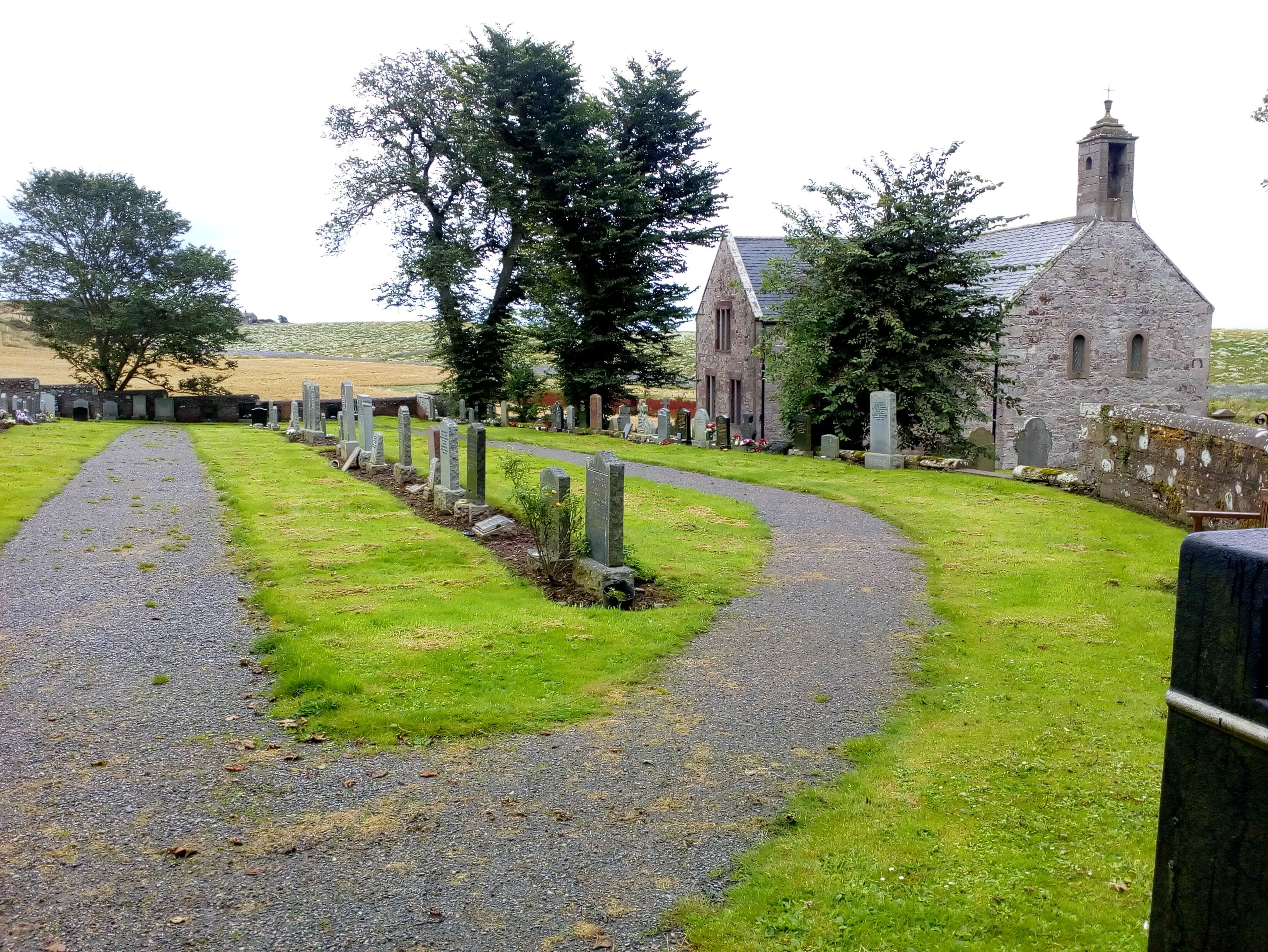 A cemetery with a winding path, stone headstones, and a church with a stone tower.
