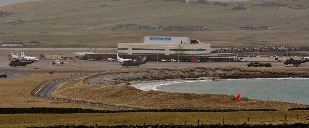 An airport with multiple helicopters, a runway, and a coastal landscape.