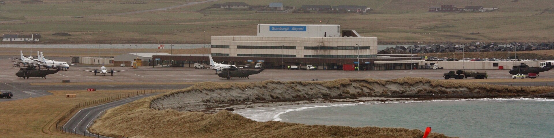 An airport with multiple helicopters, a runway, and a coastal landscape.
