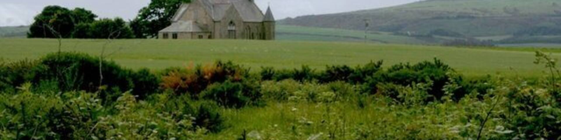A church in a rural landscape with rolling hills in the background.