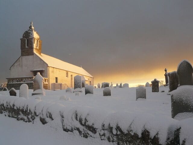 A church surrounded by snow-covered gravestones.