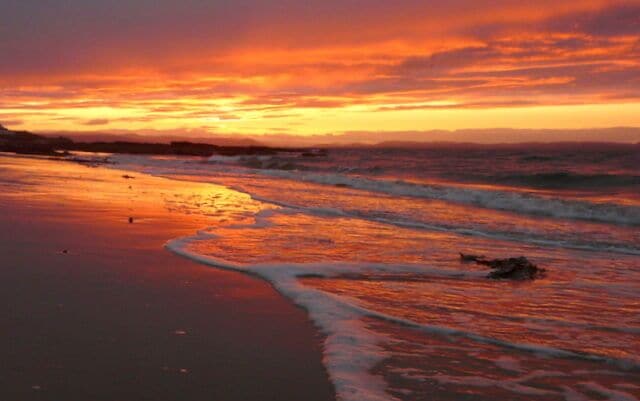 A beach at sunset with waves and a colorful sky.