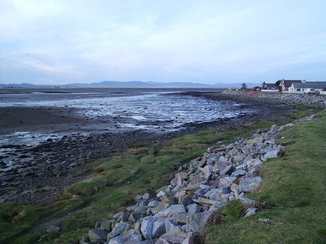 A rocky shoreline with a grassy area and a building in the distance.