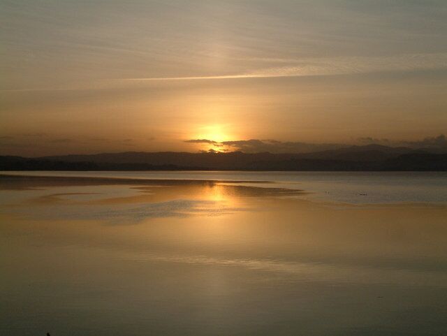 A sunset over a calm lake with a clear reflection of the sun.
