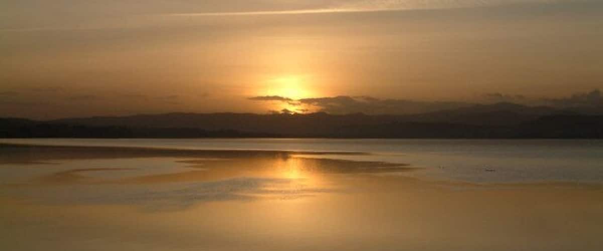 A sunset over a calm lake with a clear reflection of the sun.