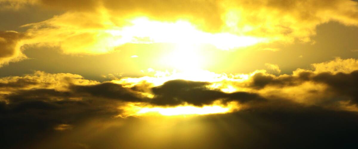 A sunset with the sun shining through clouds.