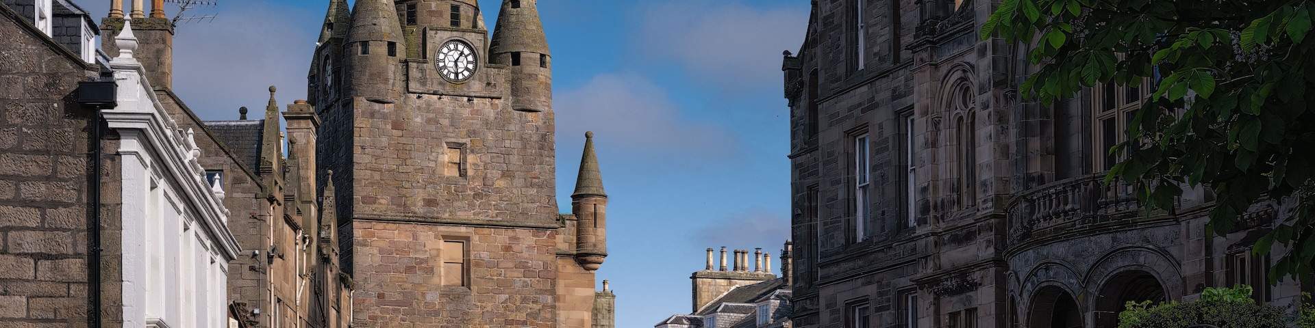 A historic stone tower with a clock, surrounded by traditional buildings and a clear blue sky.