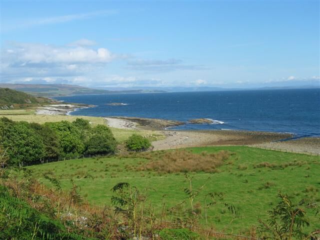 A coastal landscape with a grassy foreground, a rocky shoreline, and the ocean in the background.