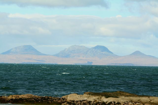 A body of water with rocky shores and distant mountains under a cloudy sky.