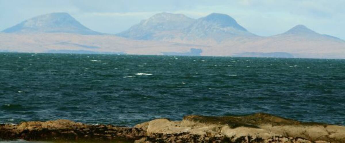 A body of water with rocky shores and distant mountains under a cloudy sky.