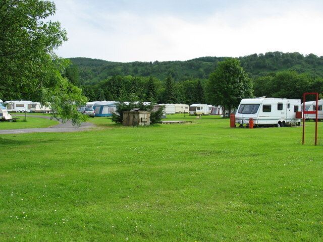 Un camping con vehículos recreativos y tiendas de campaña, rodeado de colinas verdes.