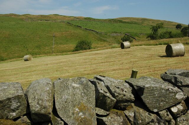 A rural landscape with rolling hills, stone walls, and hay bales.