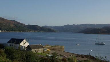 A coastal town with a harbor, a sailboat, and rolling hills in the background.