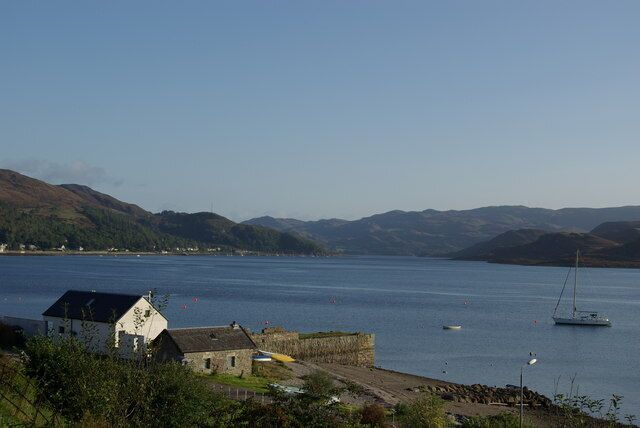 A coastal town with a harbor, a sailboat, and rolling hills in the background.