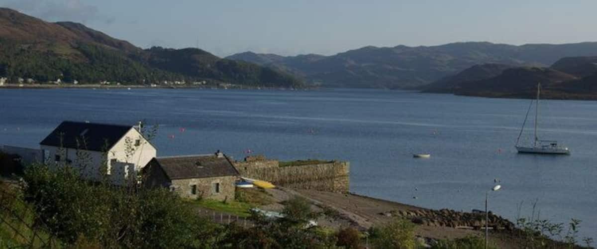 A coastal town with a harbor, a sailboat, and rolling hills in the background.
