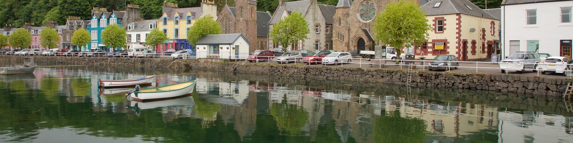A calm harbor with boats, colorful buildings, and a church with a tall spire.