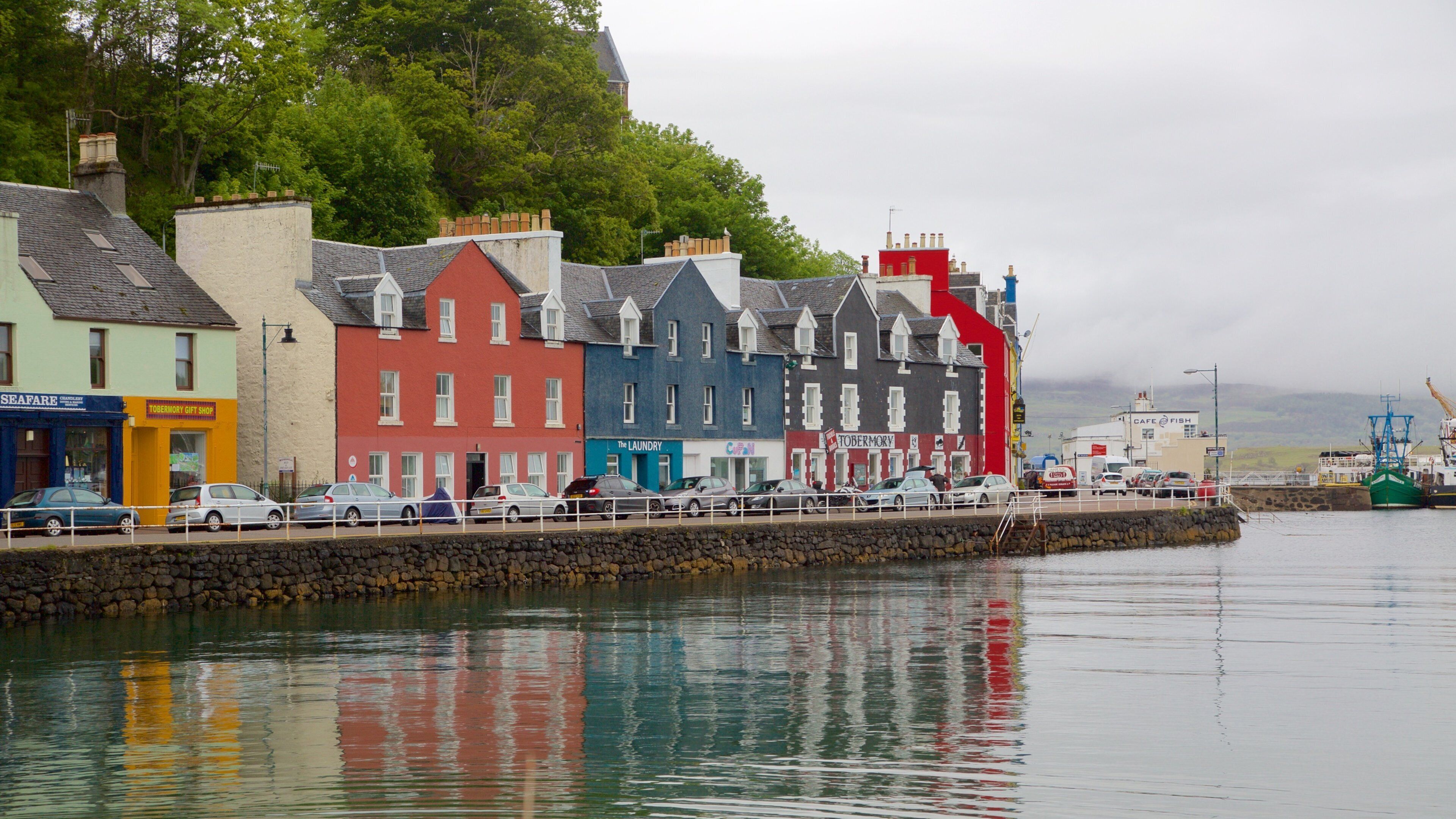 A waterfront with colorful buildings, a stone wall, and a fishing boat.