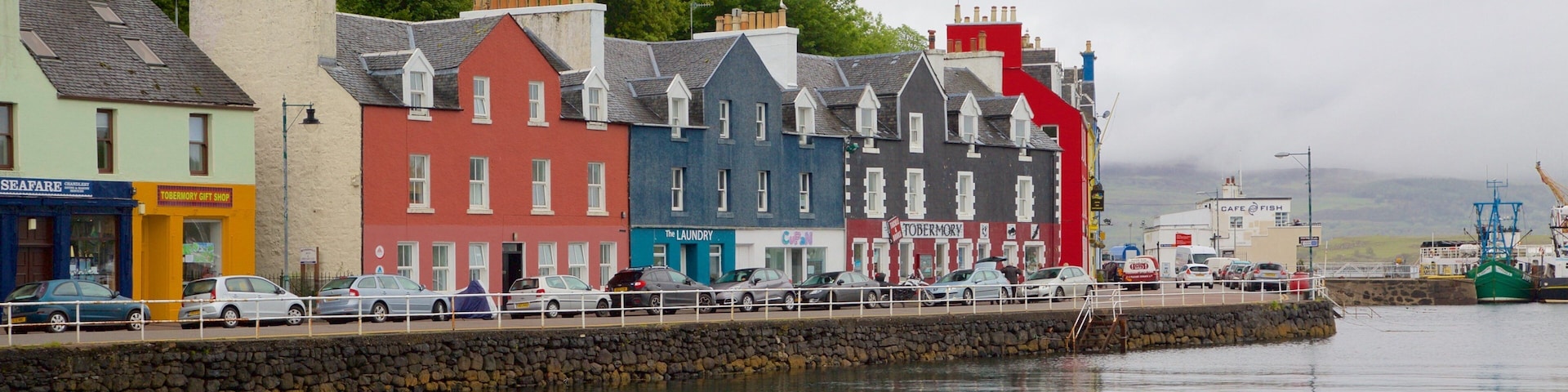 A waterfront with colorful buildings, a stone wall, and a fishing boat.