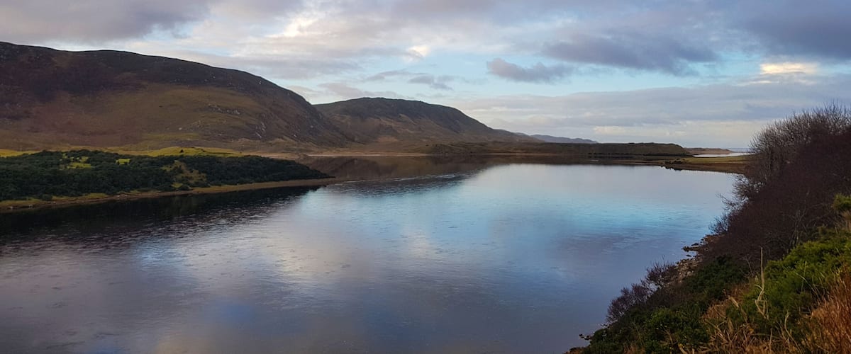 A calm lake surrounded by hills and a cloudy sky.