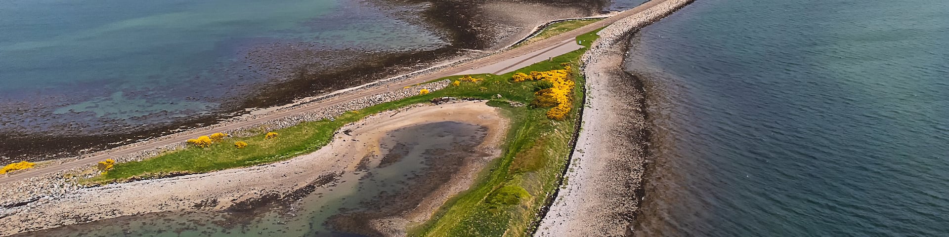 A coastal landscape with a curving road, a rocky shoreline, and distant mountains.