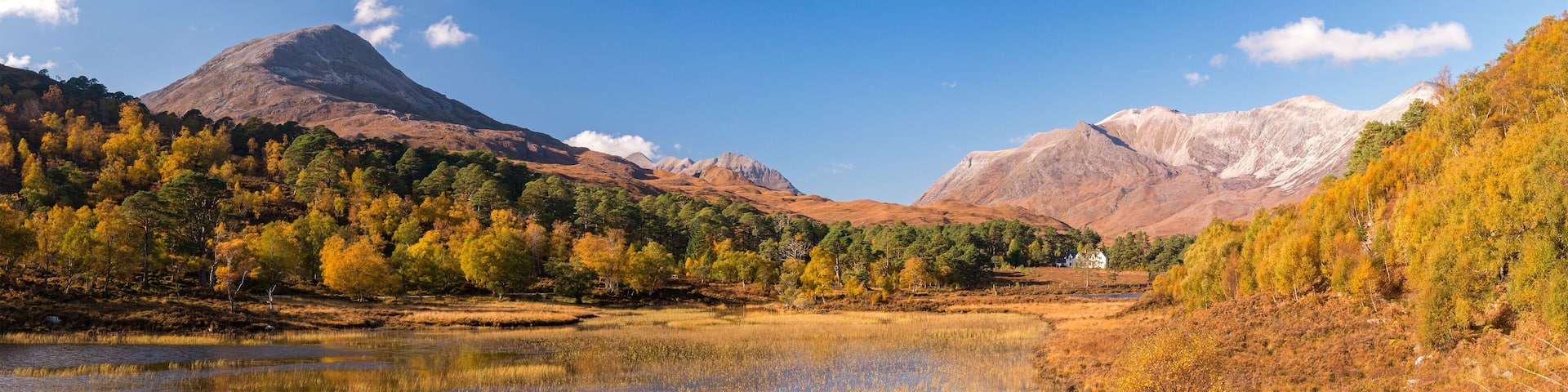 A mountainous landscape with autumn-colored trees, a lake, and a small house in the valley.