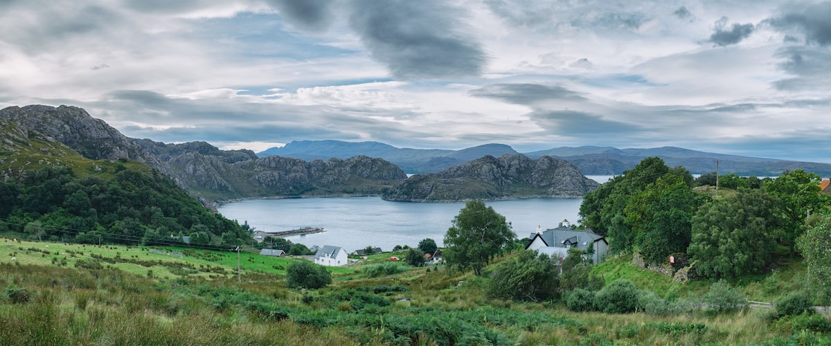 A coastal landscape with rugged mountains, a lake, and scattered houses.