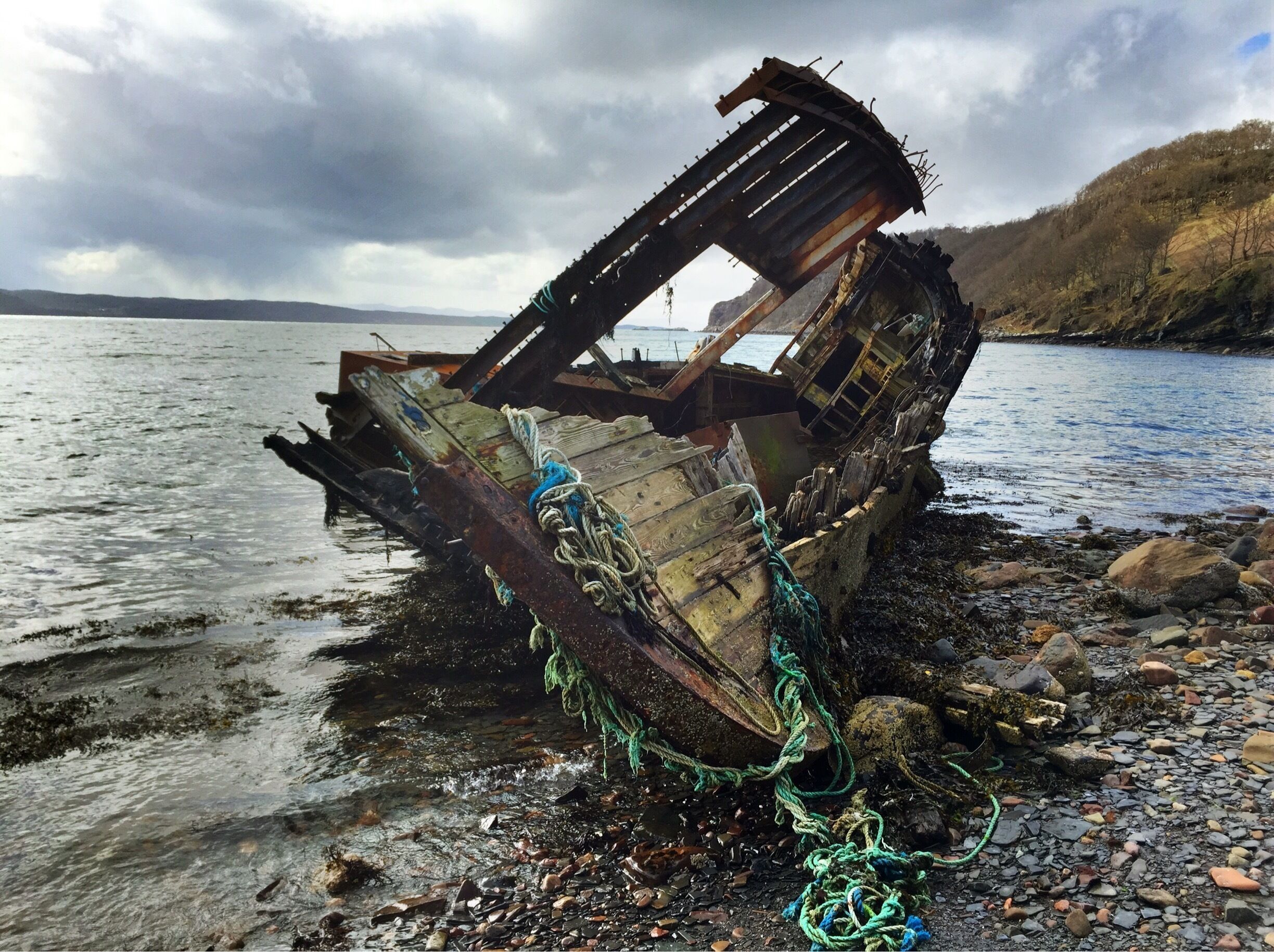 A sunken shipwreck on a rocky shore with overcast skies.