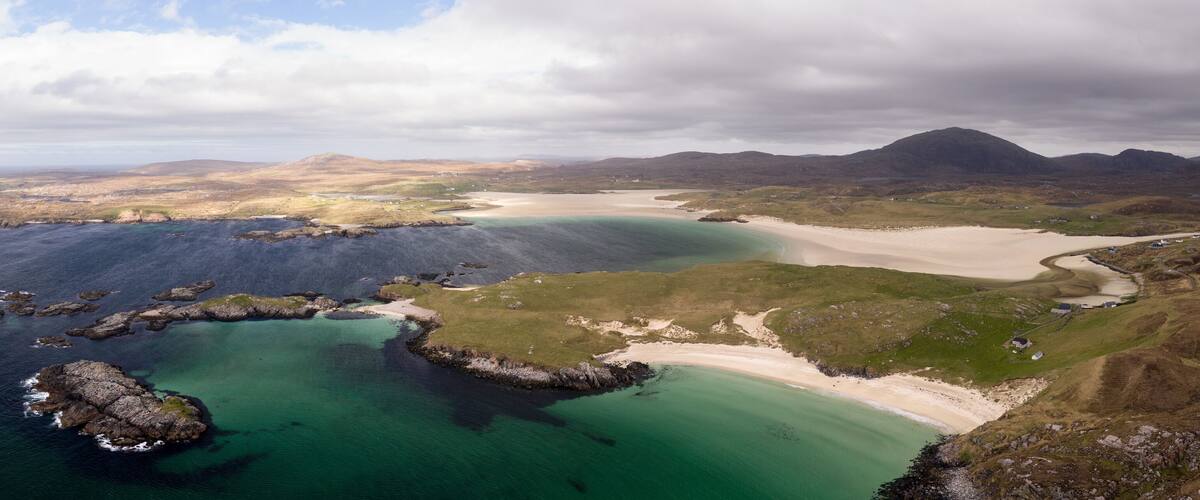 A coastal landscape with a sandy beach, rocky outcrops, and a mountainous backdrop.