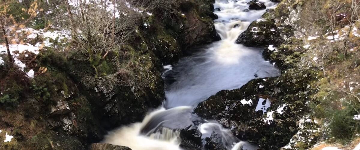 A fast-flowing mountain stream with rocky banks and patches of snow.