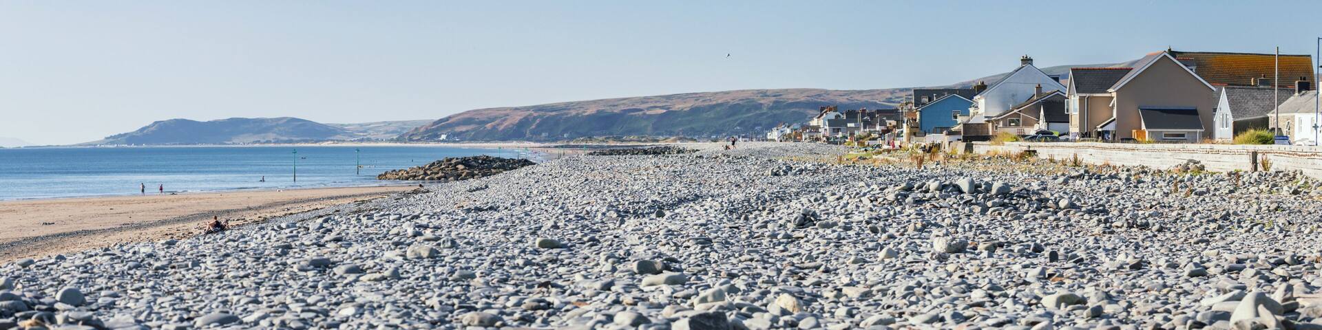 A pebble beach with houses and a clear blue sky.