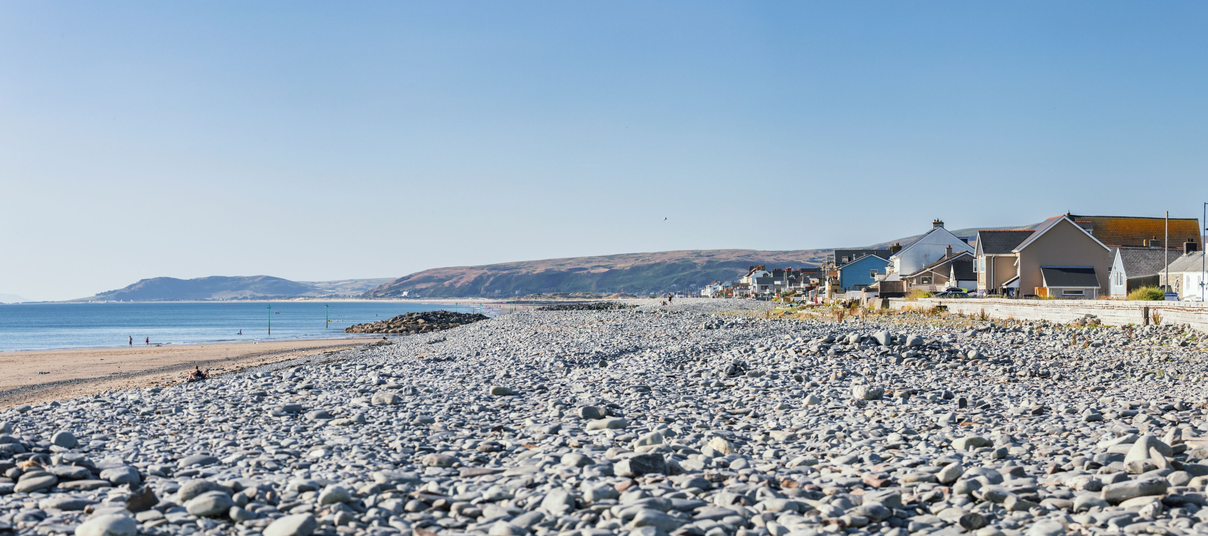 A pebble beach with houses and a clear blue sky.