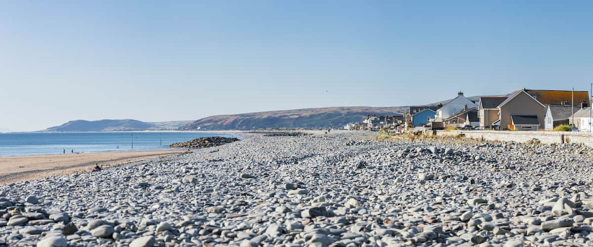A pebble beach with houses and a clear blue sky.