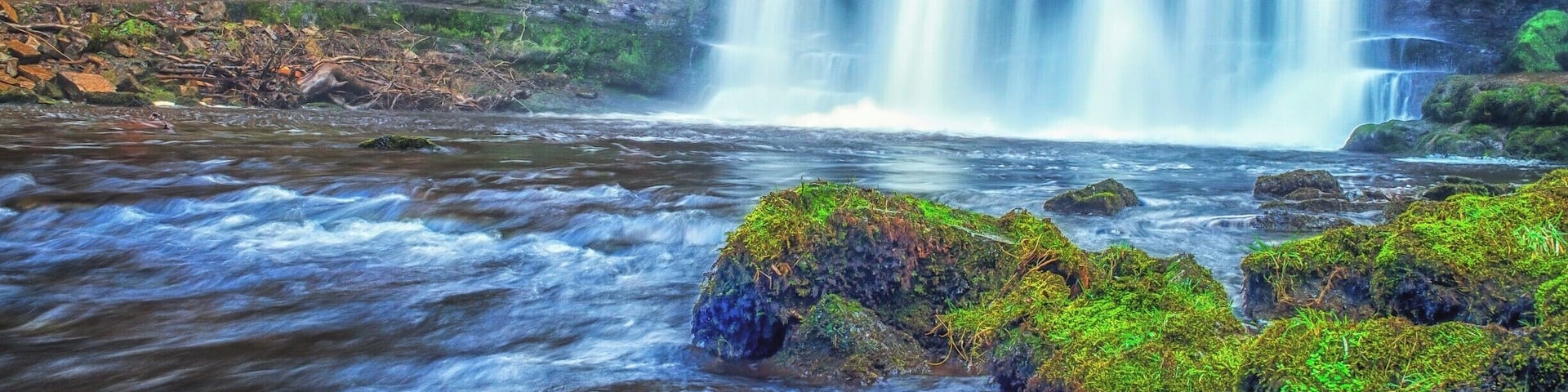 A waterfall cascading over moss-covered rocks into a river.