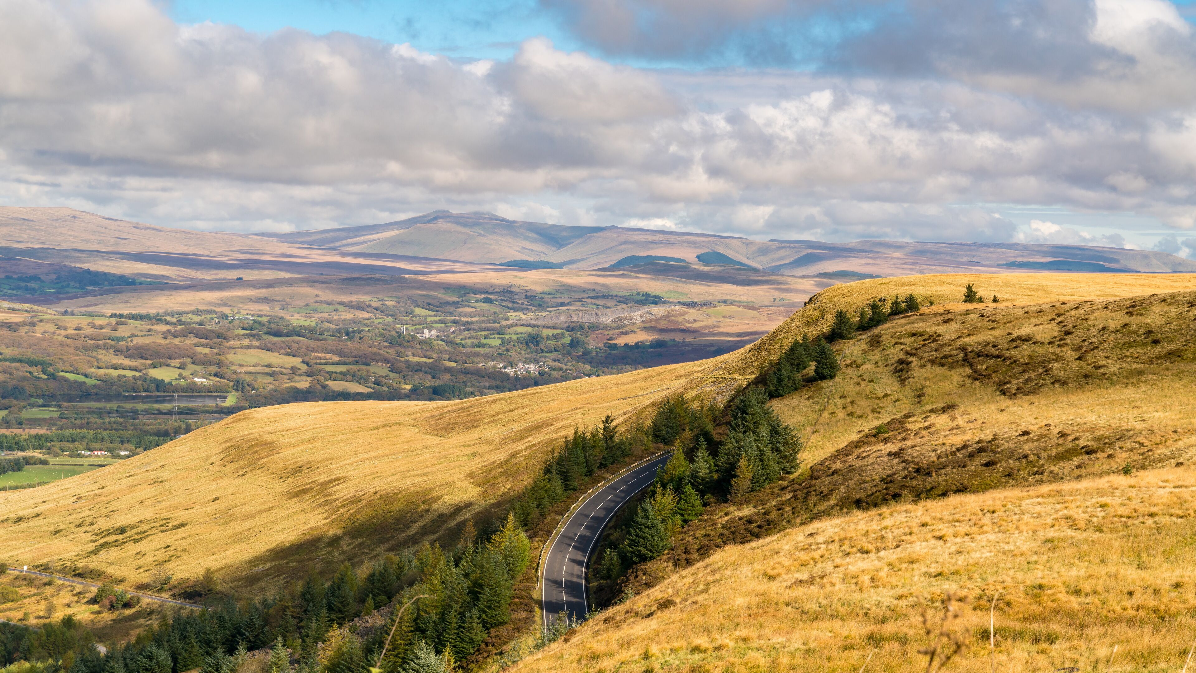 A winding road through rolling hills with a valley in the background.