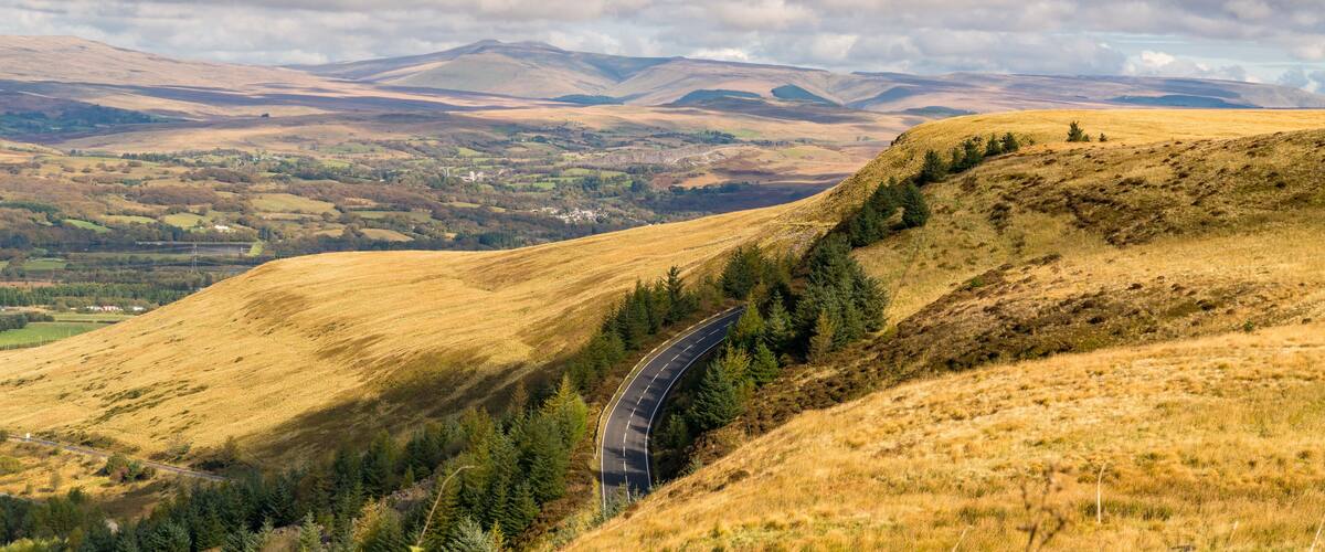 A winding road through rolling hills with a valley in the background.