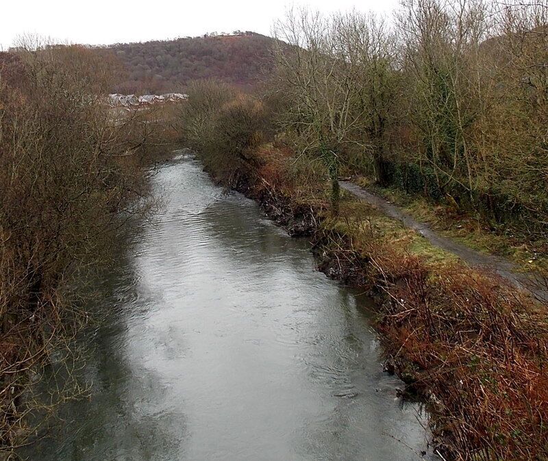A narrow river with surrounding vegetation and a path on the right.