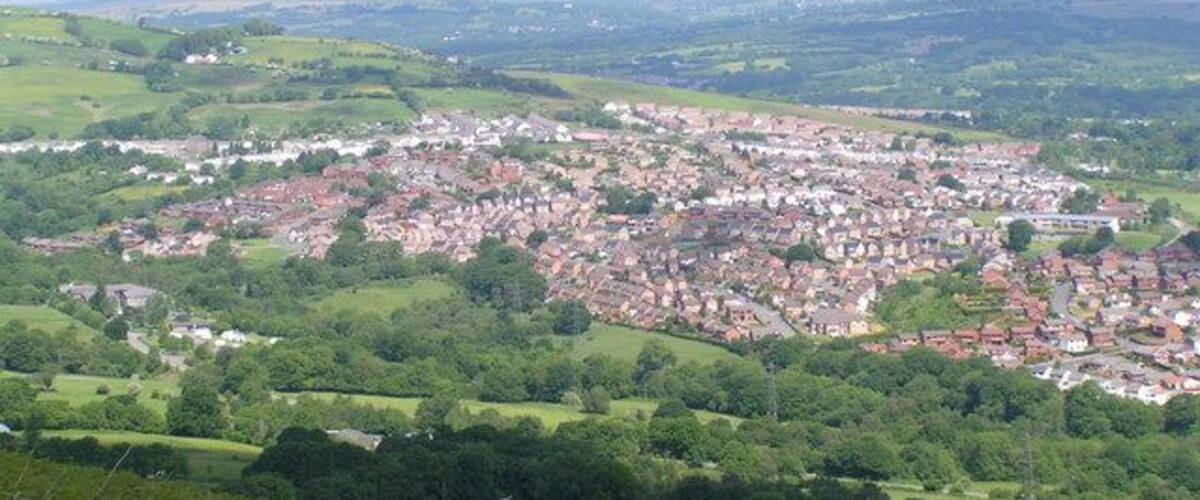 Uma cidade aninhada em um vale, com colinas ondulantes e um rio ao primeiro plano.