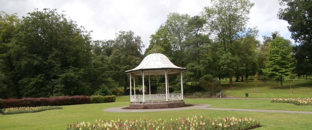 A gazebo in a park with a flower bed in the foreground.