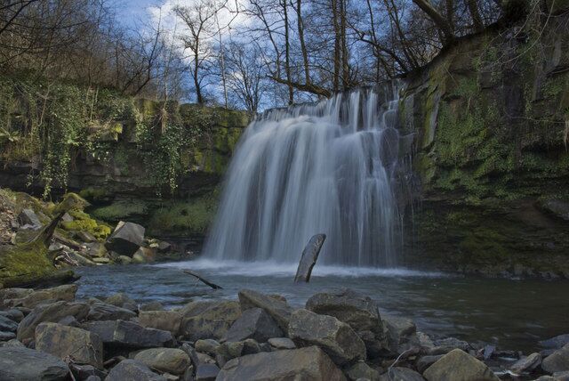 Una cascada fluye sobre rocas en un área boscosa.