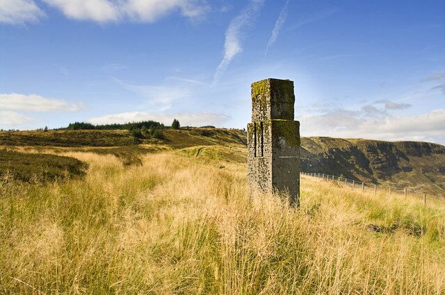 Una piedra vertical en un campo cubierto de hierba, con colinas al fondo.
