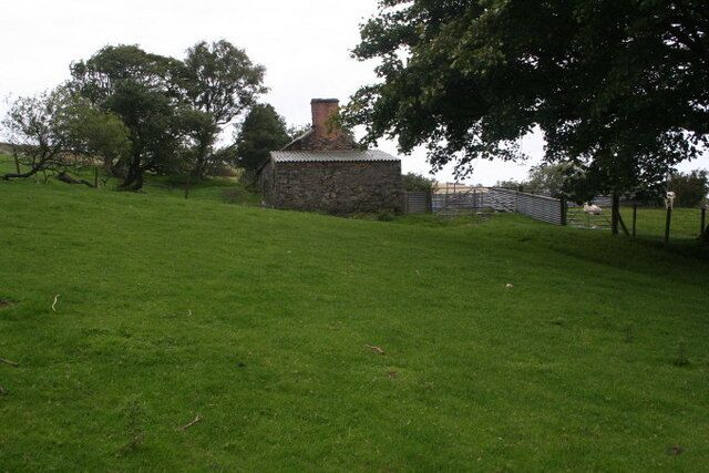 A stone building with a chimney, surrounded by a grassy field and trees.